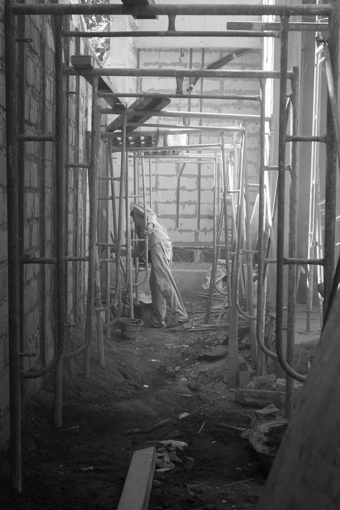 A lone worker amidst scaffolding in a dimly lit construction site.